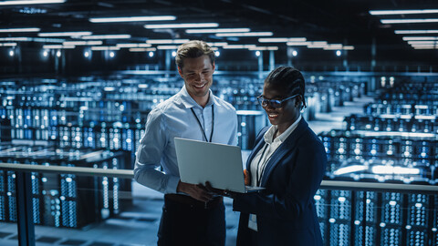 Two people smiling while one is holding laptop in datacenter.