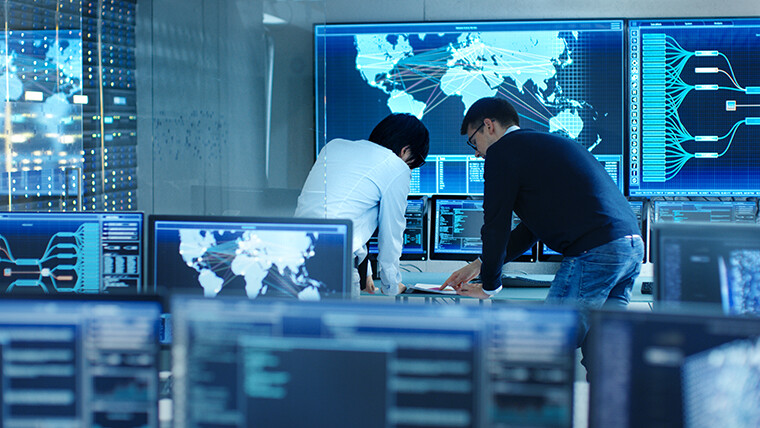 People standing at computer monitors with global maps