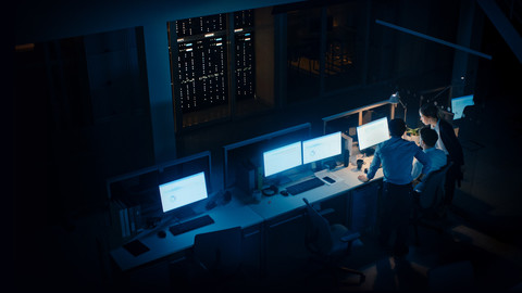A dark server room with multiple people looking at monitors
