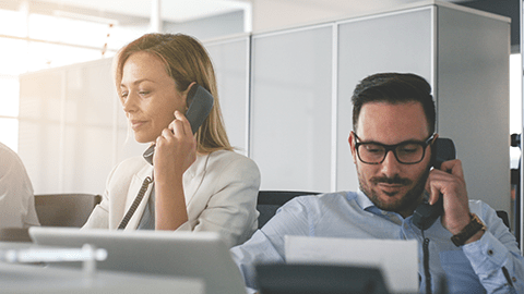 Man and woman in an office talking on phones